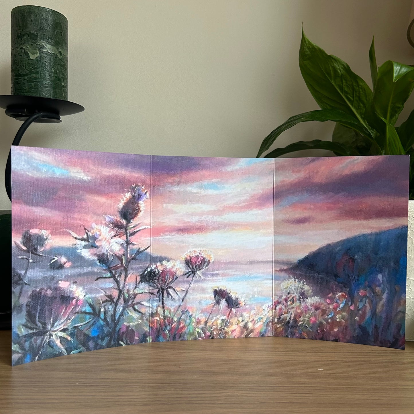 Trifold self-sealing greetings card with a painting of a sunset over the Atlantic ocean with thistles in the foreground on a wooden surface.