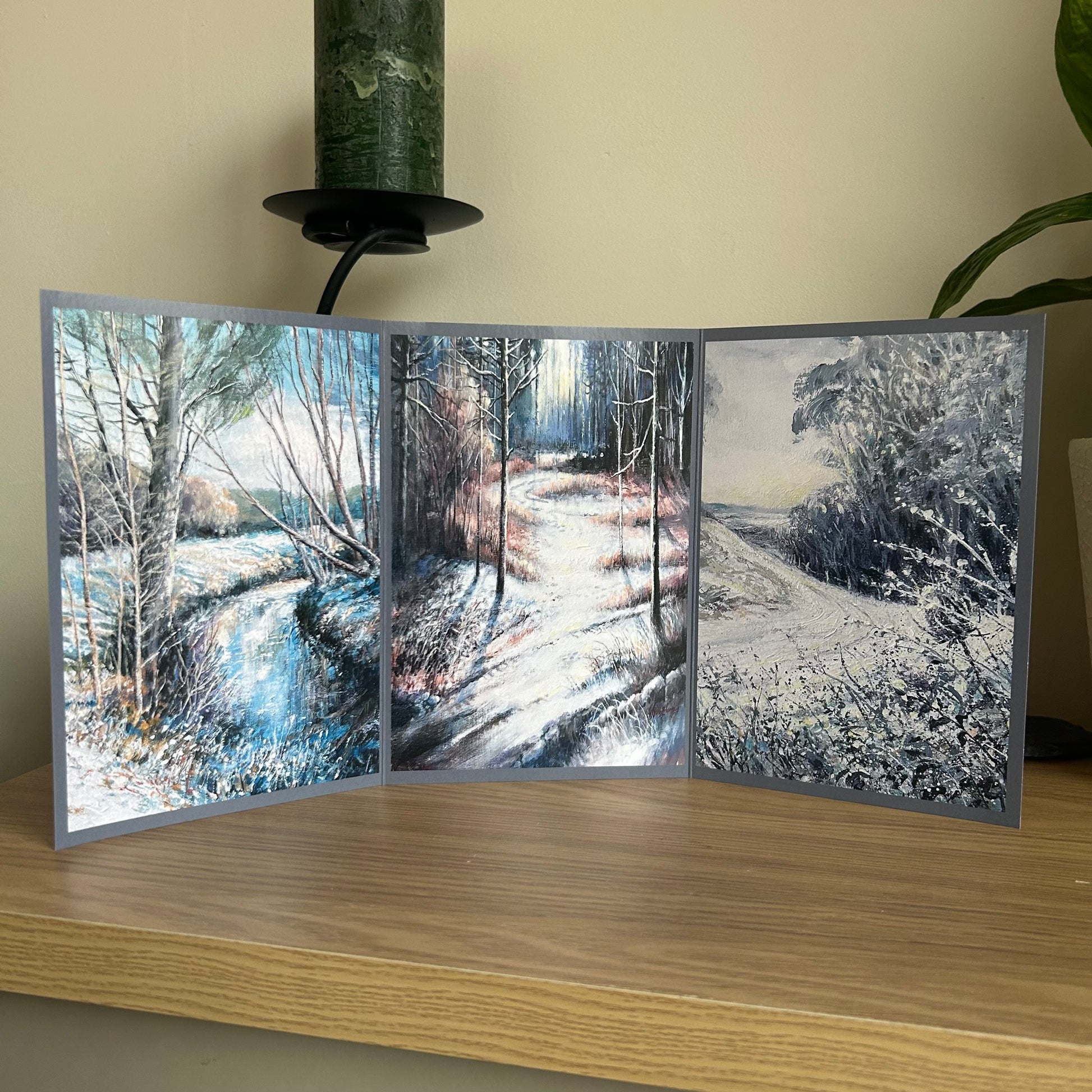Greetings card showing a triptych of winter landscapes on a wooden surface with a neutral background