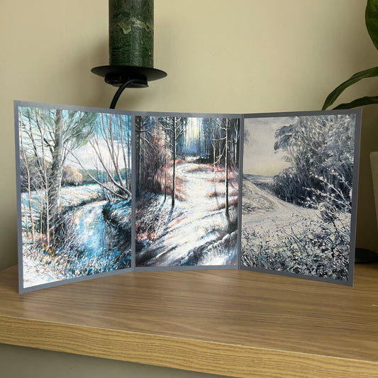 Greetings card showing a triptych of winter landscapes on a wooden surface with a neutral background