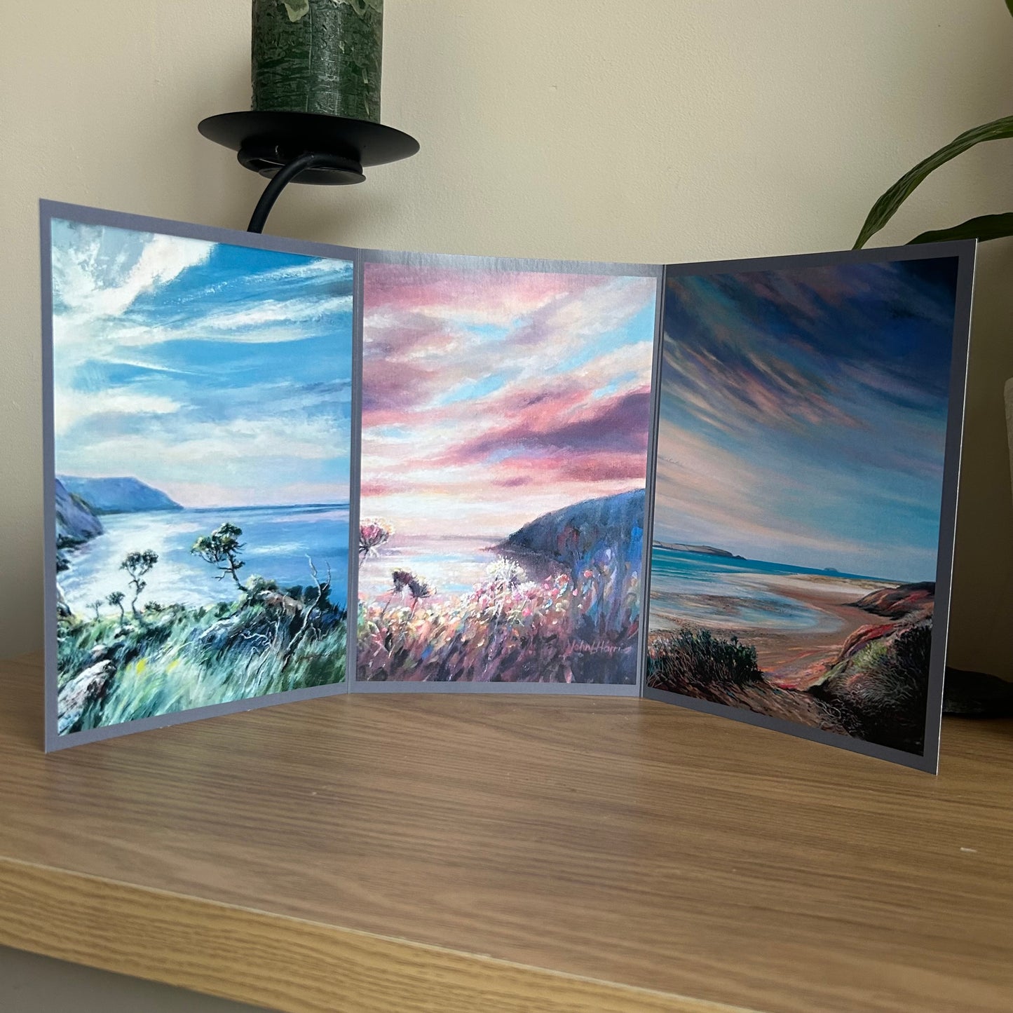 Trifold greetings card featuring a triptych of paintings of coastal scenes on a wooden surface.