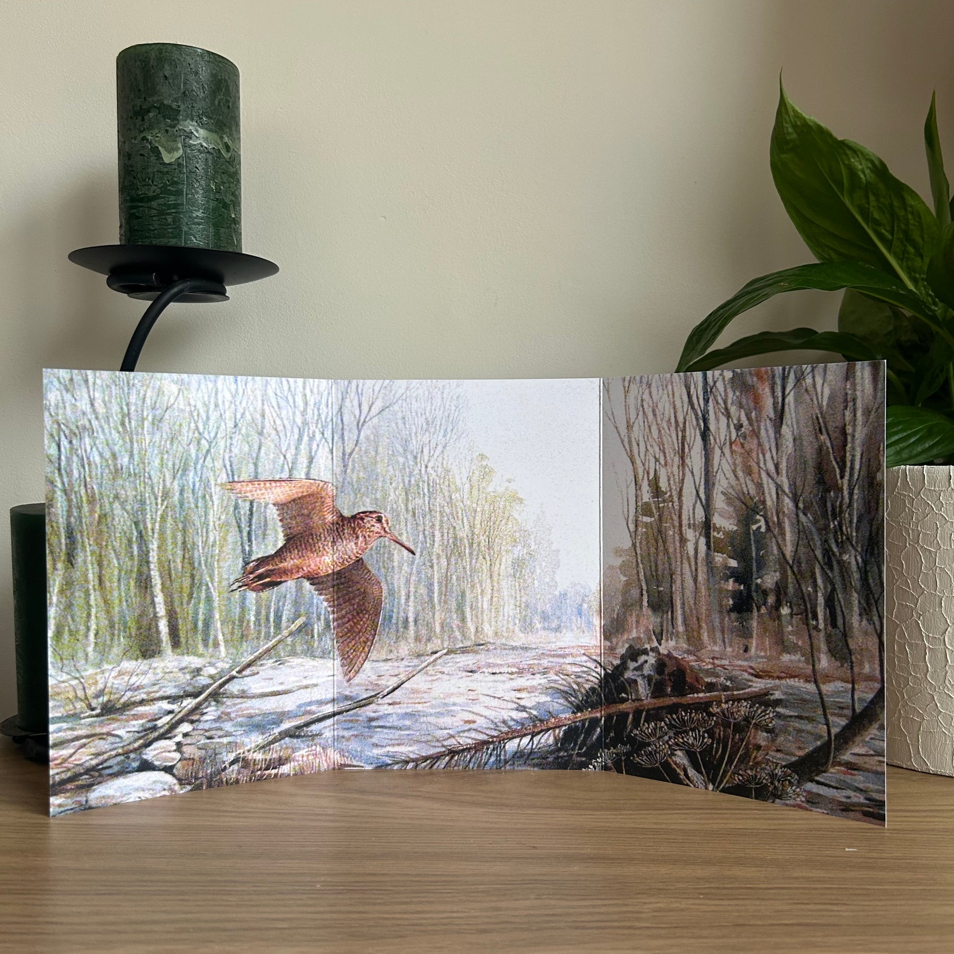 Trifold nature-themed card showing a Woodcock flying in Turnham Woods on a wooden surface with a plant and candle in the background.