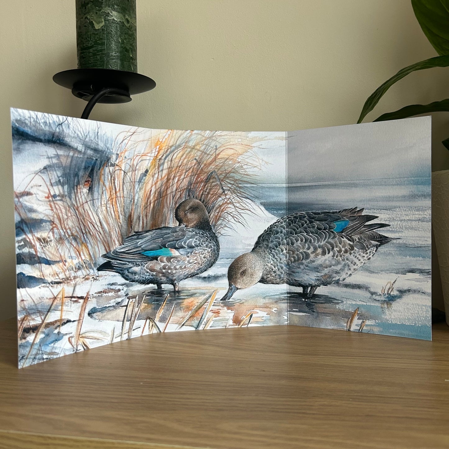 Trifold greetings card showing two Teal ducks on a snowy landscape on a wooden surface.