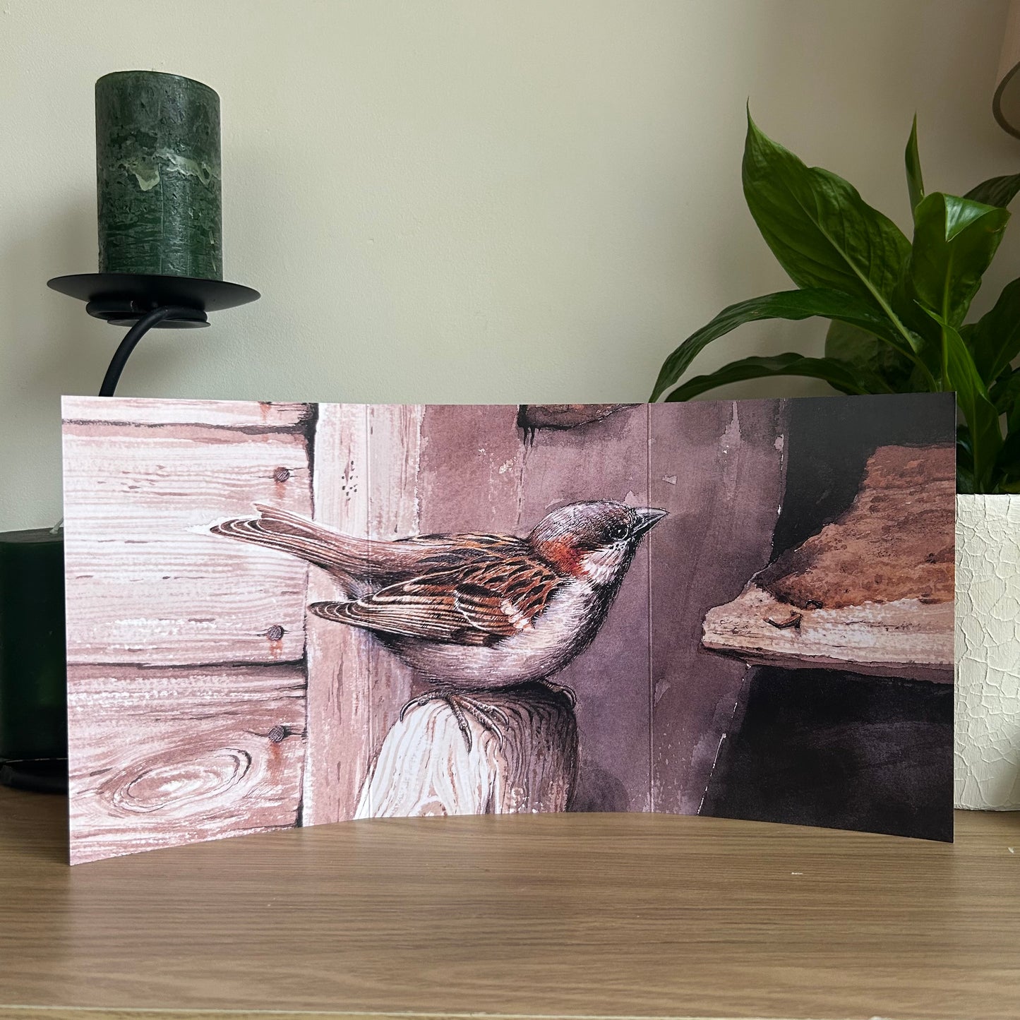 Trifold Greetings Card with a sparrow design on a wooden surface with a plant and candle in the background