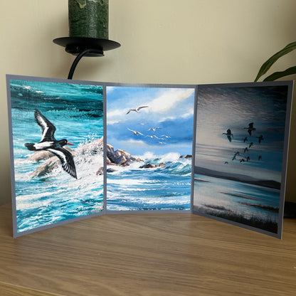 Tri-fold card with three scenic images of birds and water on a wooden surface.