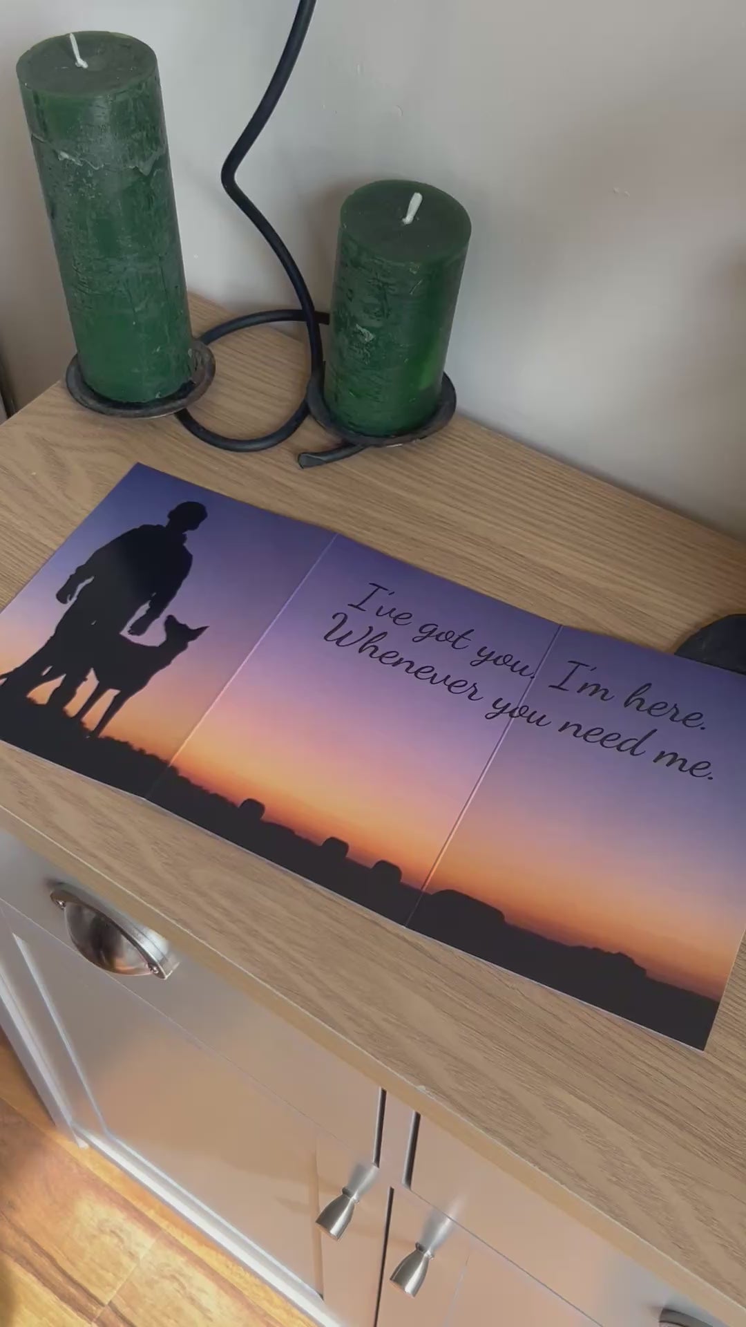 The video shows a demonstration of the Bare Cards Trifold Dog Photo Sentiment Card. The trifold image opens up to show a stunning sunset and silhouette of a dog looking up at a young boy and the caption "I've got you. I'm here. Whenever you need me". The video then shows how to fold and seal this unique card to form the built-in envelope depicting sunset over a field of corn.