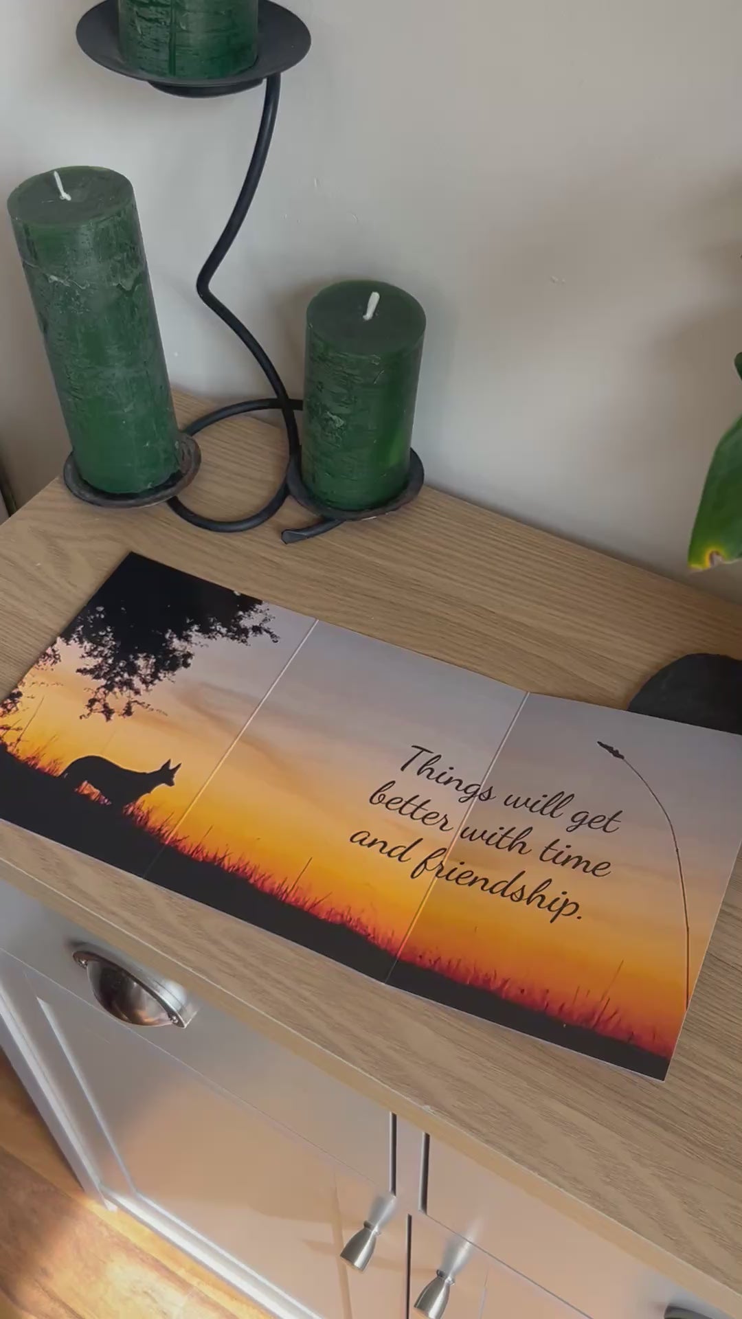 The video shows a demonstration of the Bare Cards Trifold Dog Photo Sentiment Card. The trifold image opens up to show a stunning sunset and silhouette of a dog under a tree and the caption "Things will get better with time and friendship". The video then shows how to fold and seal this unique card to form the built-in envelope depicting sunset over a field of corn.
