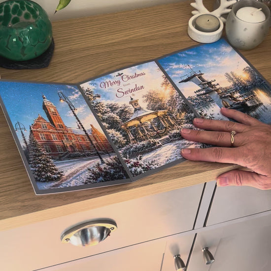 Demonstration of the Bare Cards Christmas Card for Swindon, showing how to write, fold seal, open and display the self-sealing card. This triptych card shows  festive images of The Town Hall, the pavillion in Old Town Gardens and the diving board Coate Water.